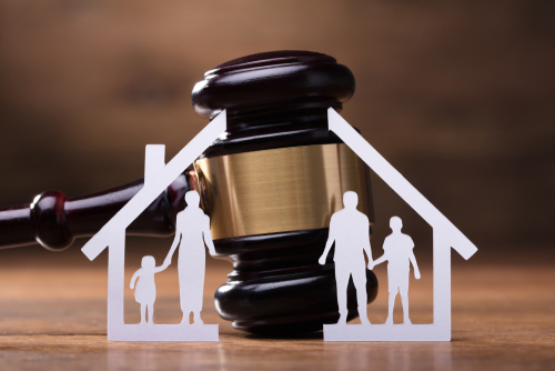 Paper cutout family inside a house outline placed in front of a judge’s gavel, symbolizing family law and protection.